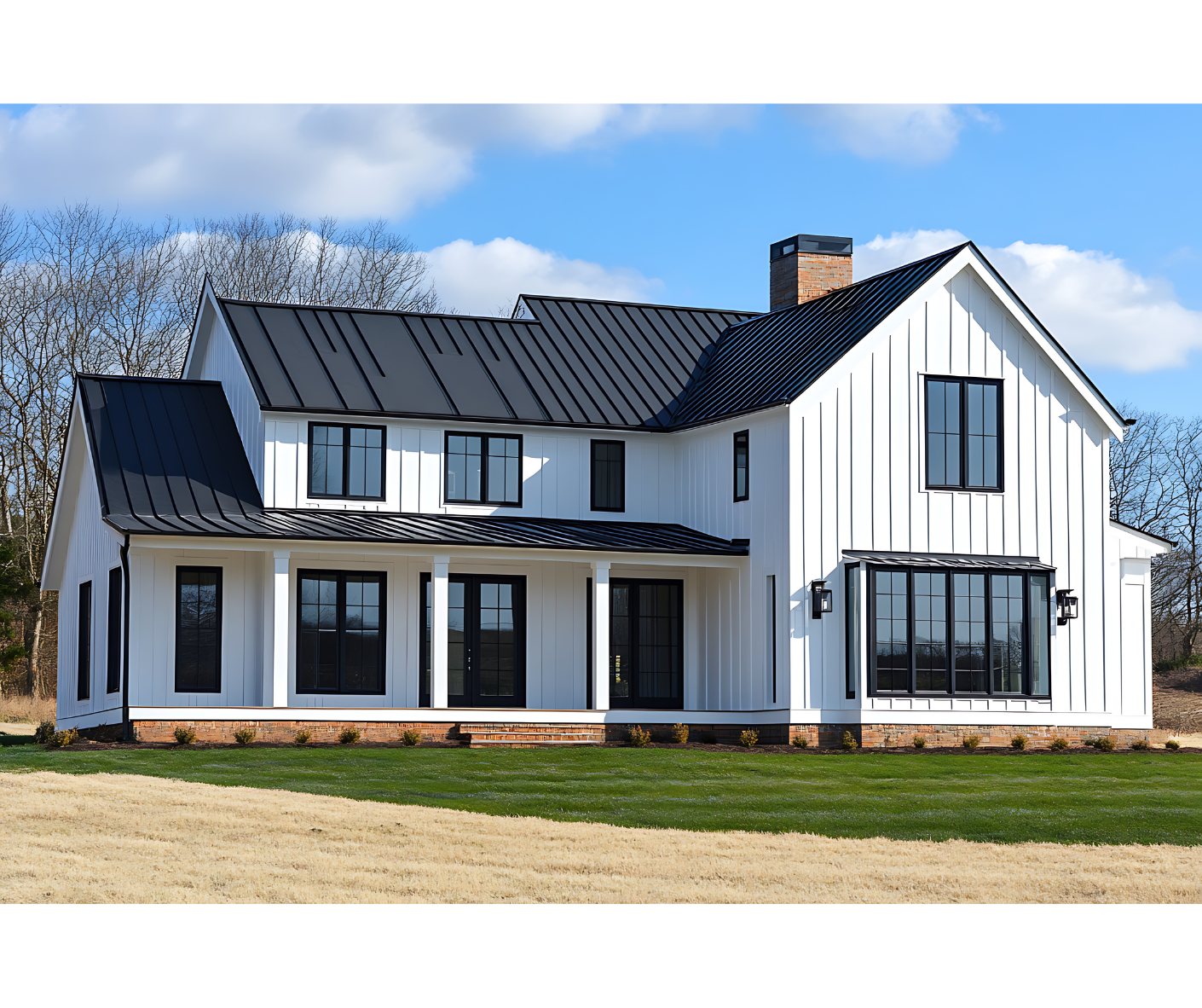 White farmhouse with black roof and trim on a grassy lot under a blue sky.